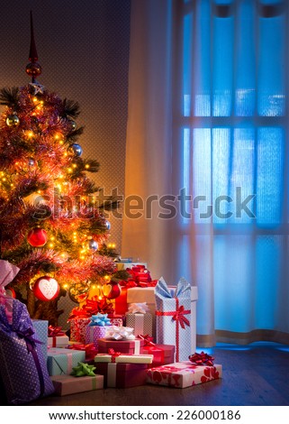 Christmas eve\'s night with colorful gifts and tree with lights.