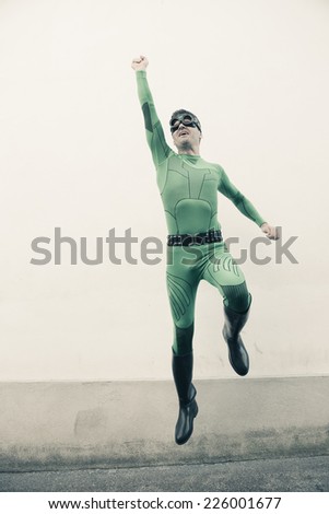 Green funny superhero with costume and mask flying with fist raised.