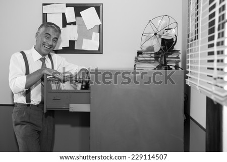 Cheerful smiling employee in 1950s style office searching for a file in the cabinet.