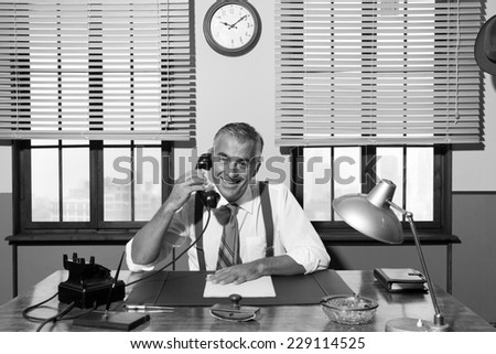 Smiling handsome businessman on the phone working at desk, 1950s vintage office.