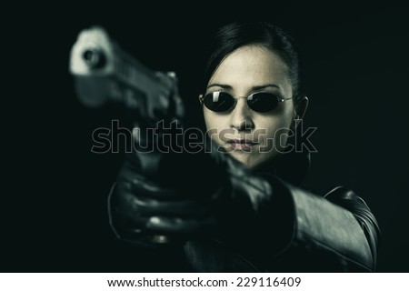Attractive female criminal in black leather coat pointing a gun.