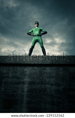 Green confident superhero standing against a cloudy sky with arms akimbo.