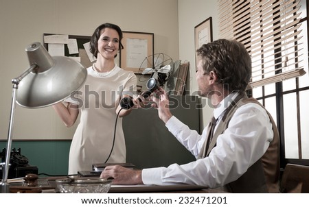 Smiling secretary passing phone receiver to her director, 1950s vintage style office.