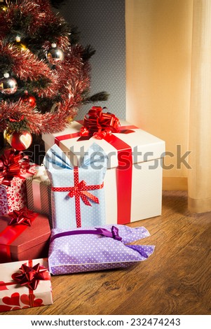 Colorful gift boxes with ribbon and christmas tree with baubles next to a window.