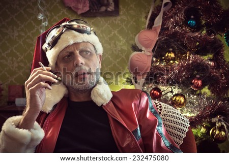Portrait of Bad Santa smoking a cigarette with sexy bra hanging on Christmas tree on background.