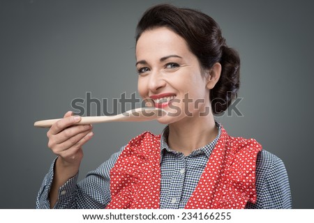 Smiling female cook tasting a recipe with a wooden spoon