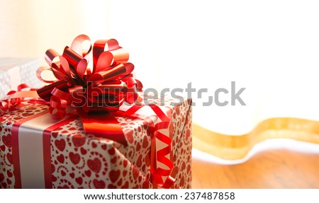Red and white gift box close-up with huge ribbon next to the window.