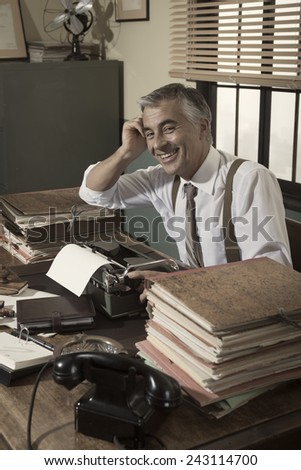 Cheerful vintage office worker sitting at desk and smiling at camera.