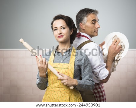 Smiling strong woman with rolling pin watching her husband cleaning dishes