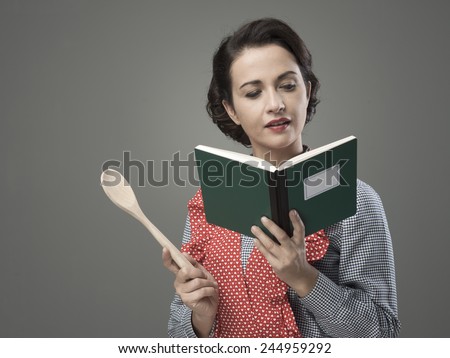 Smiling vintage woman holding an open cookbook and a wooden spoon