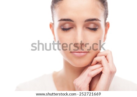 Beautiful young woman touching her radiant face skin with eyes closed on white background