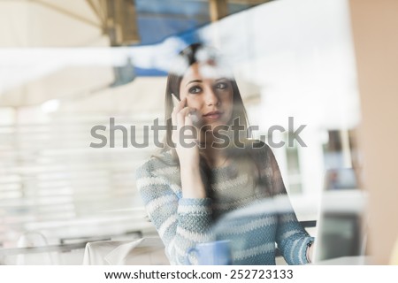 Young woman having a phone call and working at computer next to a window
