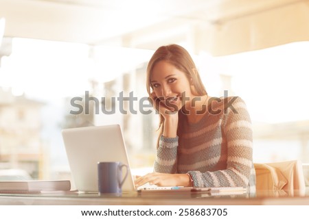 Smiling young woman working at office desk with her laptop