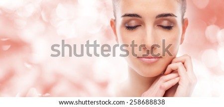 Beautiful young woman touching her radiant face skin with eyes closed
