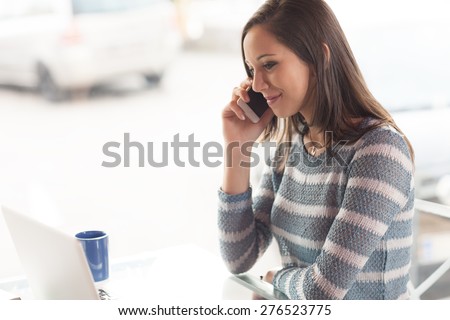 Beautiful young girl having a phone call sitting next to a window