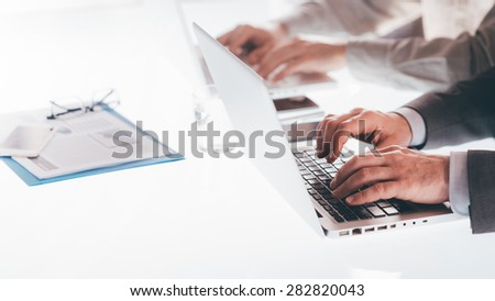 Professional businessmen working on laptops at office desk, hands close up, unrecognizable people