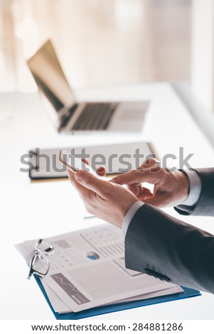 Businessman in his office texting with a smartphone, desktop and laptop on background, mobile communication concept