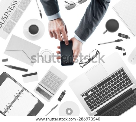 Businessman using a touch screen smartphone, desktop with laptop on background, top view