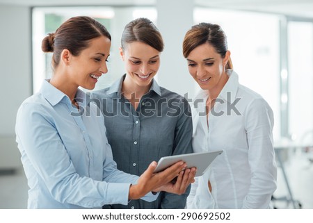 Professional smiling business women standing in the office and using a touch screen tablet, they are enjoying and watching the screen