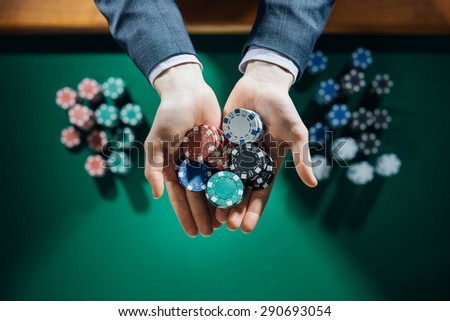 Elegant male casino player holding a handful of chips with green table on background, hands close up top view