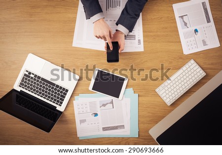 Businessman working at office desk hands top view with laptop and financial reports: he is using a mobile touch screen smart phone