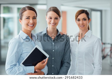 Professional smiling business women standing in the office and smiling at camera, one is holding a digital tablet