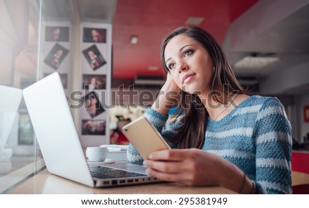 Teen girl with laptop texting with her mobile phone and leaning on a table