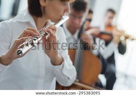 Professional female flustist playing her instrument on stage with classical music symphony orchestra