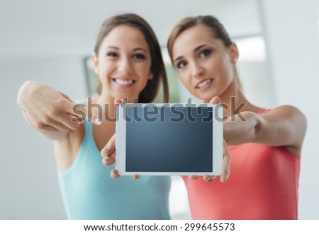 Cheerful teenager girls showing a tablet and pointing, they are smiling at camera