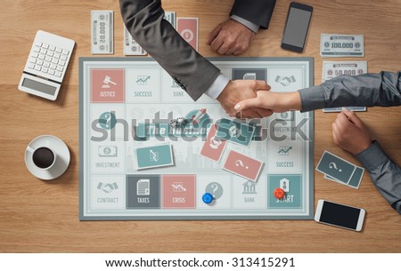 People playing a business board game on a wooden table, hands shaking close up, partnership and agreement concept