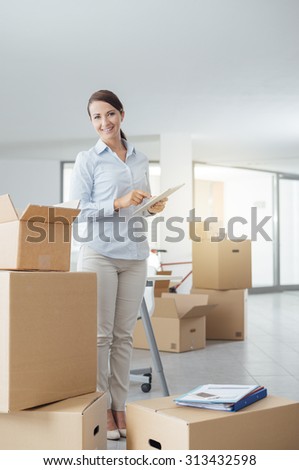 Businesswoman moving in her new office surrounded by cardboard boxes, she is holding a digital tablet