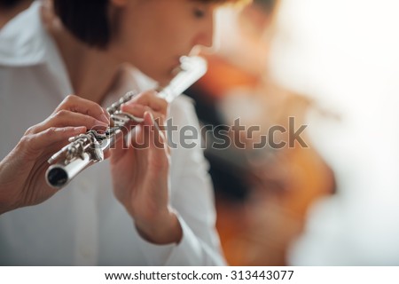 Professional female flute player performing with classical music symphony orchestra, unrecognizable person
