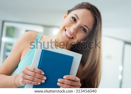 Smiling college student holding books and looking at camera, learning and education concept