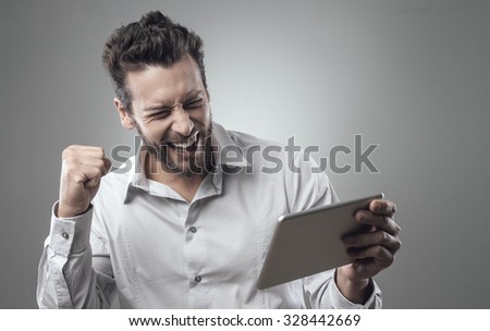 Cheerful smiling man receiving good news on tablet with fist raised