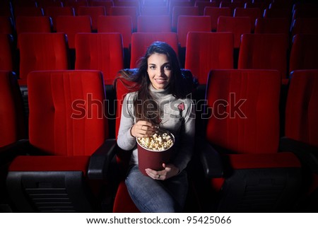 portrait of a pretty young woman sitting in an empty theater, she eats popcorn and smiles, front view