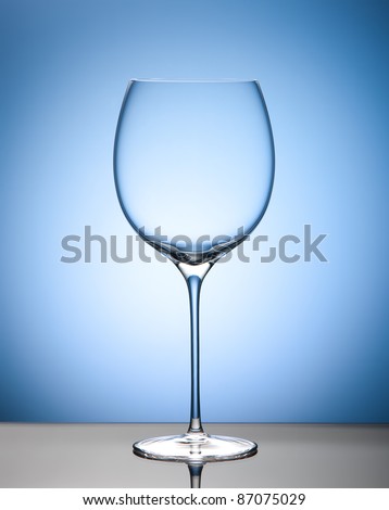 Empty wine glass on blue background and mirror surface