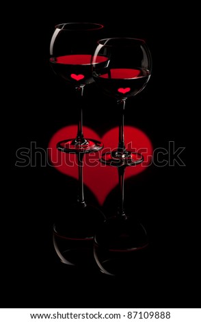 Two wine glasses on red heart and black background with red hearts in the water