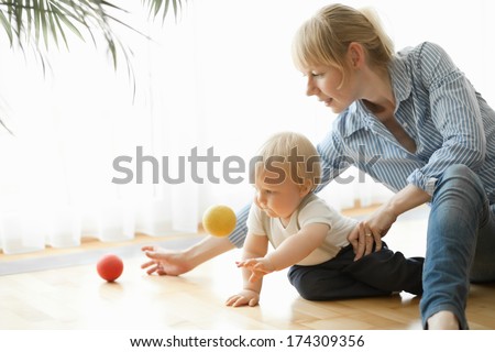 Happy mother and her 1 year old son playing with small ball at home.
