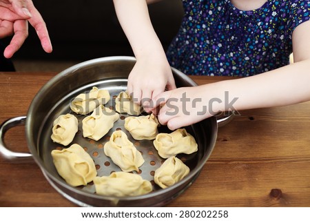 Cooking together with children. Little girl leaning how to make manti (Central Asia dumplings). Manti are ready to be loaded in steamer for cooking.