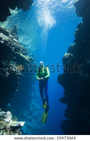 a pretty female scuba diver swimming between two coral cliffs, underwater