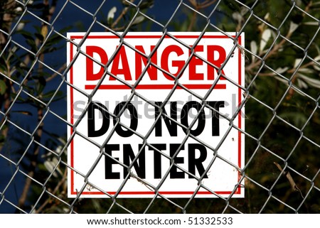 White sign with Red and Black writing saying Danger Do Not Enter and attached to a wire fence. There are spiders webs and plant material on the fence and sign