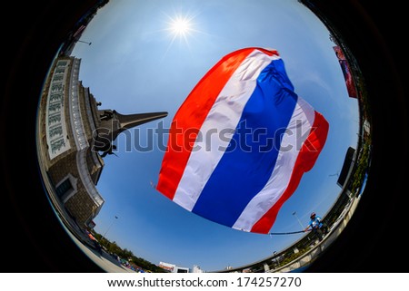 BANGKO, THAILAND - JAN 18, 2014: Anti-government protester waves a big Thai flag on the Victory monument in Bangkok
