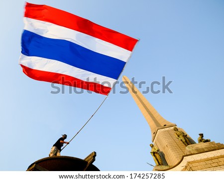 BANGKOK, THAILAND - JAN 18, 2014: Anti-government protester waves a big Thai flag on the Victory monument in Bangkok
