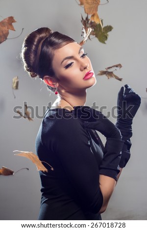 Elegant beautiful woman in a black cocktail dress and long gloves with a autumn leaves falling