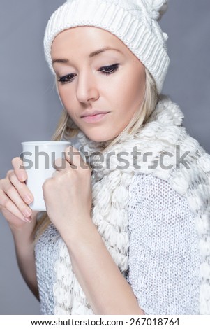 Young girl in a sweater with a white scarf and hat is holding a white cup
