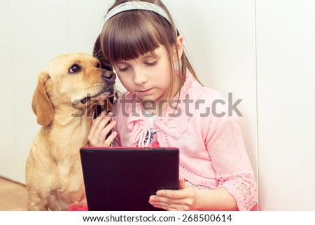 Cute little girl with a yellow dog playing on a tablet