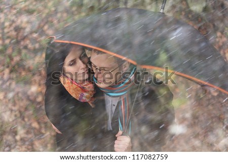 Autumn portrait of a man and a woman under an umbrella in the rain, wind storm protection