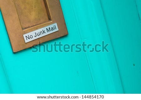Brass letterbox on a colorful turquoise blue door bearing the sign No Junk Mail
