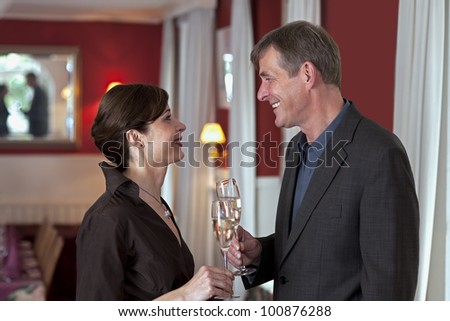 Smiling attractive middle-aged couple standing in romantic red interior with glasses of sparkling white champagne.
