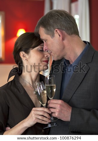 Amorous couple in close embrace standing clinking champagne glasses, showing devotion and trust.